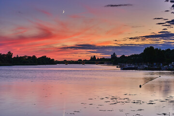 Naklejka premium Evening at the river with water and clouds and red sky and half moon