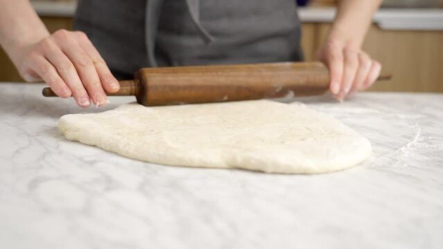 Crop baker rolling out dough in kitchen