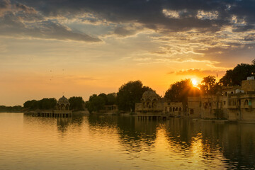 Beautiful sunset at Gadisar lake, Jaisalmer, Rajasthan, India. Setting sun and colorful clouds in the sky with view of the Gadisar lake. Connected with Indira Gandhi Canal for continuous water supply.