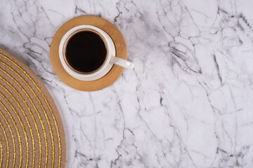 Cup of coffee with round wooden coaster on marble table background, top view