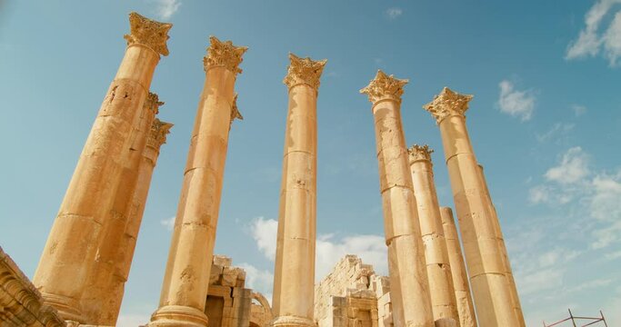 Bottom view of row of columns in Temple of Artemis in Jerash, Jordan. Ruins of pillars placed together and established as ancient architecture with sunny sky in background. 4k panning shot 