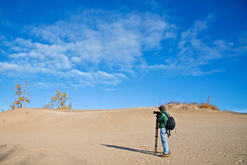 Fototapeta na wymiar A male photographer taking photos on the sand dune with blue sky and autumn leaf colour