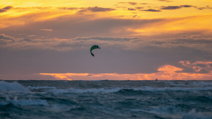 Person practicing kitesurfing in the sea, with a beautiful sunset in the background, in Castelldefels (Spain)