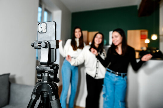 Close-up of a smartphone on a tripod filming 3 young white girls dancing, at home. Concept of making a living with videos on the Internet by being an influencer. Popularity and celebrity online