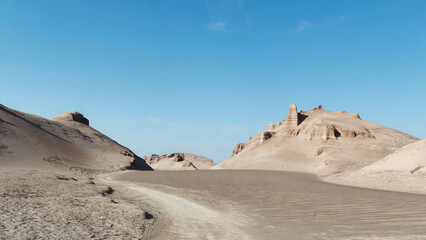 Low-angle view of the desert path and the sand and formations known as Kaluts in the background, Dasht-e Lut Desert, Iran	