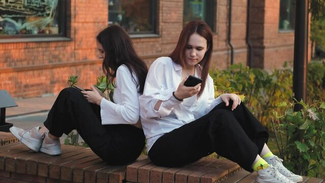 Two girlfriends are arguing, sitting on a street bench apart, young women are in conflict. Teenage friendship issues