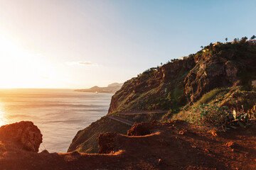 Amazing volcanic island of Madeira in the ocean at sunset. Mountains and rocks with houses and a road by the ocean with a beautiful sunset