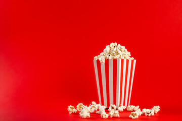 Popcorn in a red and white striped bag on a red background. Front view, copy space.