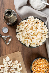 bowl with popcorn, popcorn kernels and salt and a gray napkin, on a wooden table, top view, selective focus.