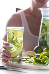 A woman holding a tall glass of cucumber infused water with ingredients beside.
