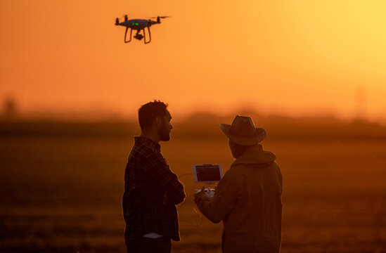 Silhouettes of farmers driving drone at sunset