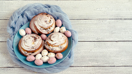 Easter eggs and decor on fresh buns with spirals with white icing sugar.