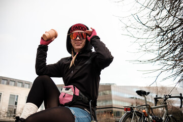 Bike courier is sitting outside holding a cup of coffee and looking at camera.