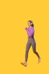 Ecstatic woman wearing sportswear is running over yellow background.