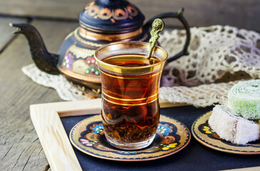 Traditional Turkish tea set: glass cup of tea, painted copper teapot, Turkish delight on a plate on wooden background