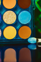 A palette of various colorful bright eyeshadows. Women's decorative cosmetics details and backgrounds. Makeup products. Professional makeup set. Female beauty concept. Blue yellow green orange colors.