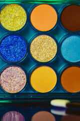 A palette of various colorful bright eyeshadows. Women's decorative cosmetics details and backgrounds. Makeup products. Professional makeup set. Female beauty concept. Blue yellow green orange colors.