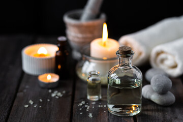 Spa setting with essential oil, candle, sea salt, pebbles, towel on dark wooden background. Massage, aromatherapy. Natural organic ingredients for relaxation, detention. Wellness in salon concept