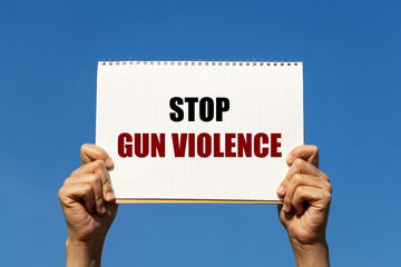Stop gun violence message on white notebook paper held by 2 hands with isolated blue sky...