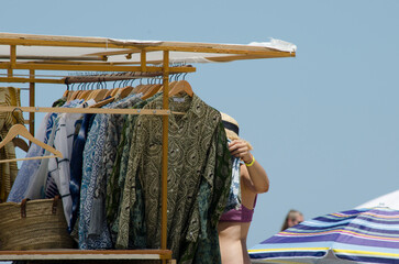 beach scene, woman choosing clothes from a cart selling beach sarongs on summer vacation