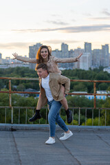Fototapeta na wymiar Young happy beautiful loving couple on a surprise romantic date on a rooftop on a Saint Valentine's Day. Attractive man and woman, male and female hugging, kissing. Sunset, skyscrapers urban view