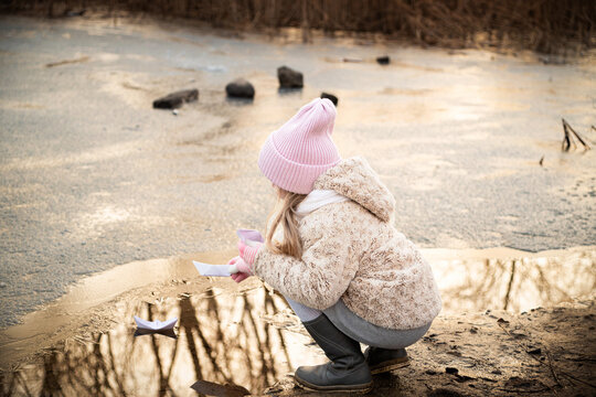 A girl lets paper boats on the shore of a pond