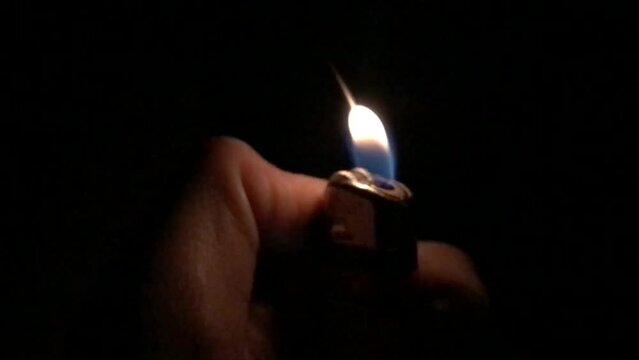 a hand holding a burning cigarette lighter. the concept of the harm of smoking