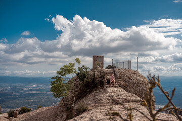 Shot of female hiker on top of Montserrat mountain in Spain. Traveler woman sitting on a stone looking at the view.
