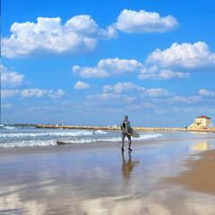 Man goes surfing on the sandy beach of the Mediterranean coast of Tel Aviv, Israel