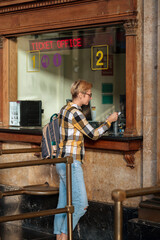 Adult 35s year old lesbian woman in plain shirt and jeans with backpack and sunglasses traveling by train in Europe. Pay with bank card for the ticket on train station in Barcelona, Spain.