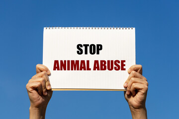 Stop animal abuse message on a white notebook paper held by 2 hands with isolated blue sky...