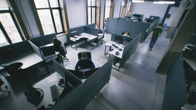 People working at office with modern design and sitting by tables with computers. Man walks corridor, comes to colleague and helps with project task. Concept of coworking. Security camera shoting.