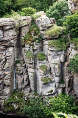 Vertical top view of huge steep rock of cliff stone in ancient granite canyon Buky (Ukraine) in summer with lot of plants, trees, moss on its surface, scenic touristic attraction, popular for climbing