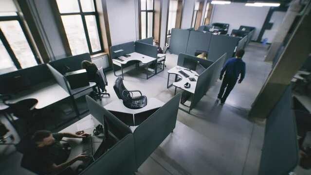 Security camera view of people working at office with modern design and sitting at the tables with computers. Woman comes to colleague and helps with project task. IT company. Concept of coworking.