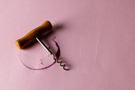 Red wine stain and corkscrew on pink background, with copy space