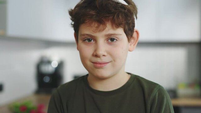 Close up portrait of the cute little boy wearing bunny ears headband sitting in the kitchen table looking at the camera. Child preparing for easter