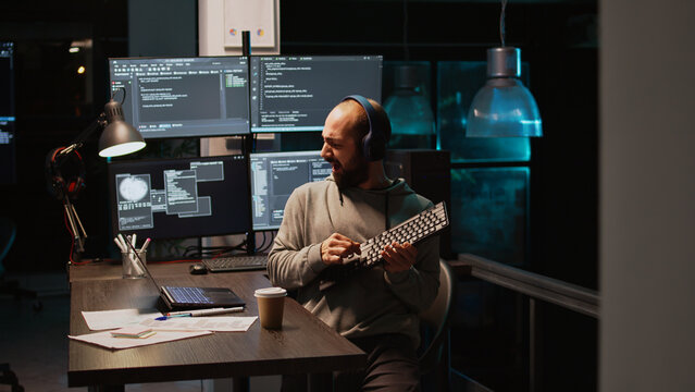 App developer playing air guitar in coding office, enjoying music and song late at night. Having fun fooling around, feeling cheerful and careless while he programs new code. Handheld shot.