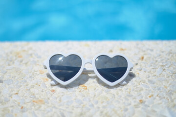 Fototapeta na wymiar white sunglasses in the shape of a heart. by the pool in a luxury hotel. The concept of summer travel, with children, holidays, holidays and family weekends.