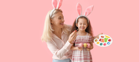 Happy little girl and her grandmother painting Easter eggs on pink background