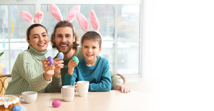 Happy parents and their little son with Easter eggs sitting at table. Banner for design