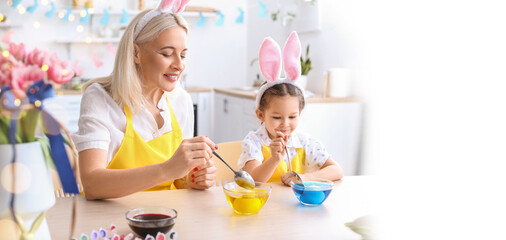 Fototapeta premium Little girl and her grandmother painting Easter eggs at home. Banner for design