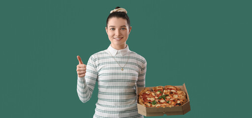 Young woman with tasty pizza showing thumb-up on green background
