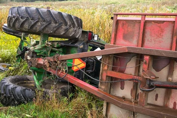 Foto op Plexiglas A farm tractor and the attached cart lay on their side in a ditch in rural Ontario Canada. © Ken