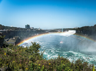A boat passes through the mist from the Falls under a rainbow in Niagara Falls Canada. The Rainbow...