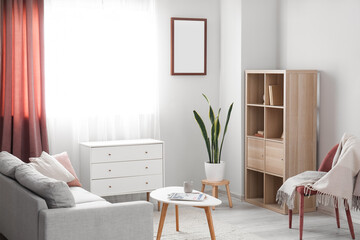 Interior of light living room with drawers, table and armchair