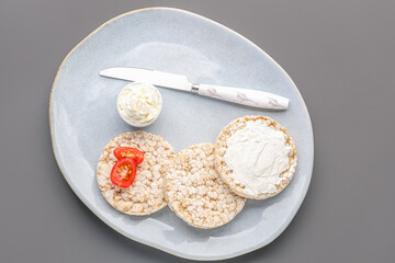 Plate with tasty crispbreads and cream cheese on grey background, closeup