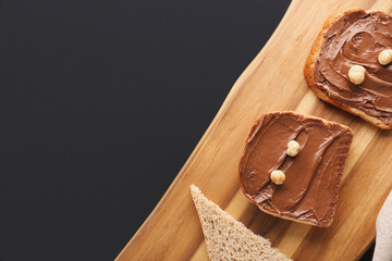 Wooden board of toasts with hazelnut butter on dark background, closeup