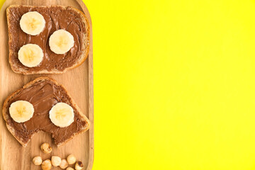 Wooden board of tasty toasts with hazelnut butter and banana on yellow background