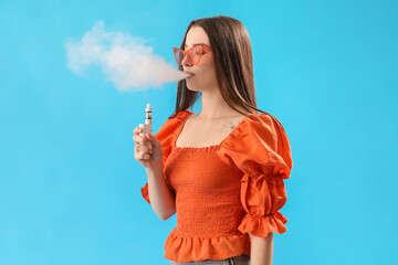 Young woman in sunglasses smoking disposable electronic cigarette on blue background