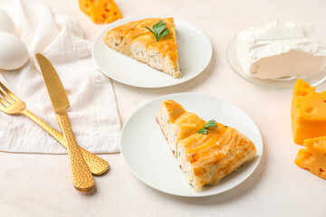 Plates with pieces of delicious cheese pie, parsley leaf, cutlery and ingredients on white table